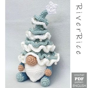 Op de afbeelding: Gehaakte kerstboomkabouter in blauw, wit en beige, versierd met parels. De kabouter heeft een witte baard, een beige neus en blauwe voeten. De boomvormige hoed is bekroond met een witte ster. De tekst "River Rice" is zichtbaar.