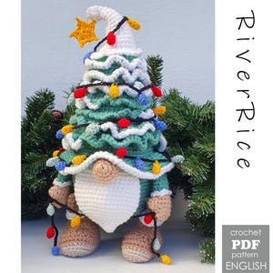 Op de afbeelding: Een handgemaakte gehaakte kerstboomkabouter met een witte baard en een ster erbovenop. De kabouter is versierd met kleurrijke lichtjes en wordt omringd door groenblijvende takken. De tekst "River Rice" staat rechts op de afbeelding.
