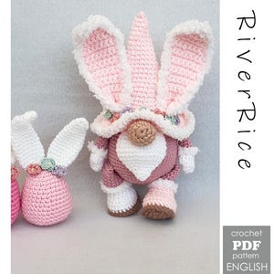 Op de afbeelding: Een gehaakte paasgnome met konijnenoren, in tinten roze, wit en bruin. De gnome heeft een lange witte baard, een roze hoed en bijpassende roze en witte kleding. De afbeelding bevat ook een gehaakt ei en de tekst "River Rice".