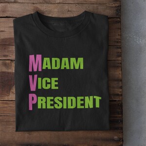 May include: Black t-shirt with the text "MADAM VICE PRESIDENT" in green and pink letters.
