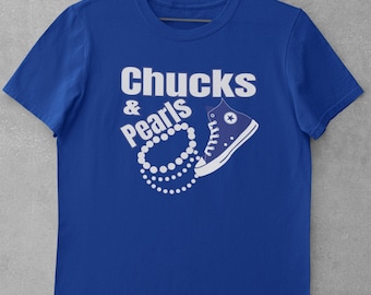 Puede incluir: Una camiseta azul real con el texto "Chucks & Pearls" en letras blancas. Un collar de perlas blancas está envuelto alrededor de una zapatilla Converse azul.