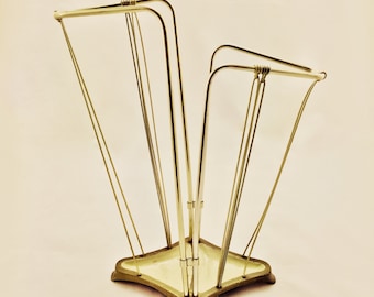 May include: A gold metal umbrella stand with a square base and multiple arms for holding umbrellas.