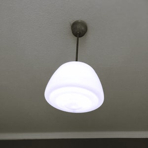 Puede incluir: Una lámpara de techo redonda y blanca con una varilla de metal que cuelga del techo.