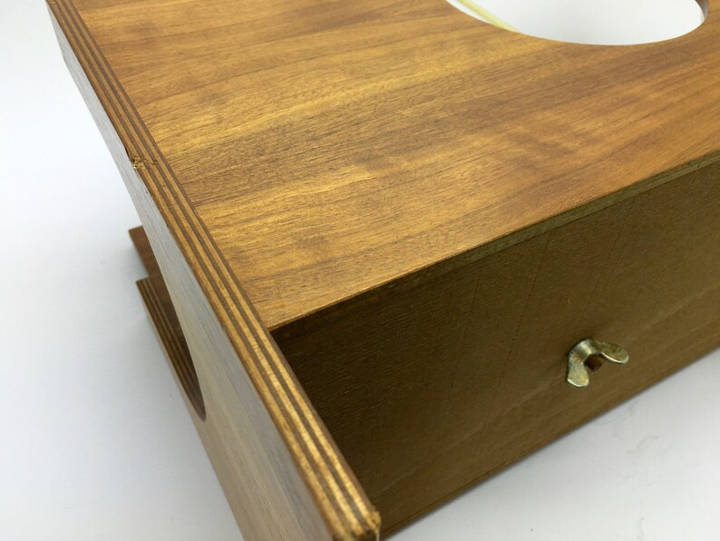 May include: A wooden box with a light brown finish. The box has a drawer with a brass wing nut and a circular opening on top. The wood grain is visible, and the box appears to be handmade.