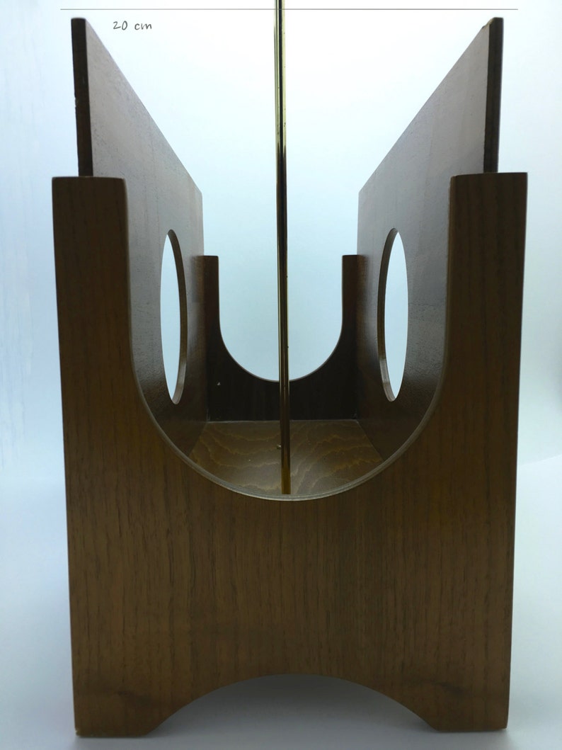 May include: A wooden magazine rack with a mid-century modern design. The rack is made of light brown wood and features two vertical panels with circular cutouts. A brass rod runs through the center. The rack is approximately 20 cm wide.