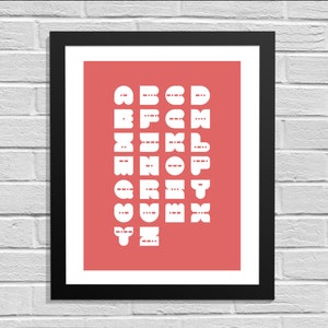 Op de afbeelding: Een ingelijst afdruk met een koraal achtergrond en witte letters die het alfabet spellen in een vet, blokachtig lettertype.