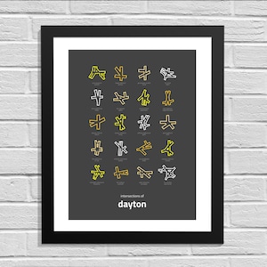 May include: A black and white framed print with a dark gray background. The print features a series of yellow and white line drawings of different road intersections. The text "intersections of dayton" is at the bottom of the print.