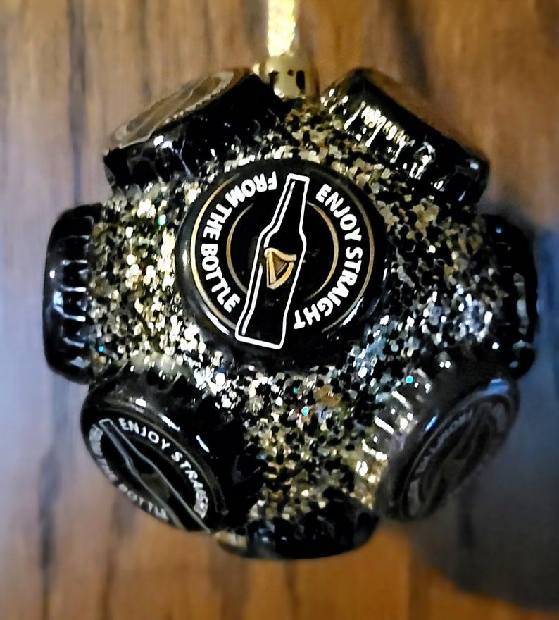 Puede incluir: Adorno navide&ntilde;o negro y dorado hecho de tapas de botellas con el texto "Enjoy Straight From The Bottle" y una silueta de una botella de cerveza.