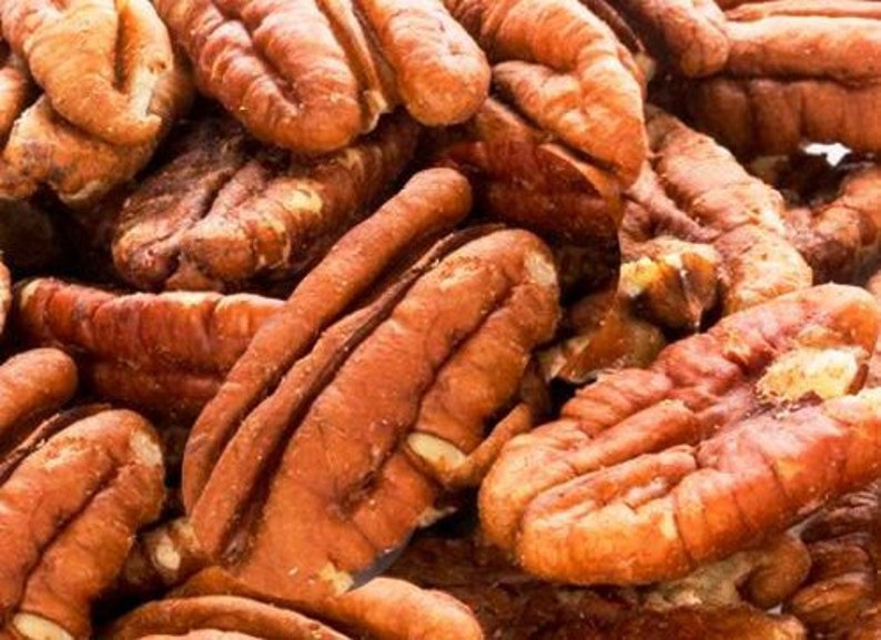 K&ouml;nnte beinhalten: Nahaufnahme eines Haufens Pekannussh&auml;lften. Die N&uuml;sse haben eine warme braune Farbe mit strukturierten Oberfl&auml;chen und sichtbaren Rippen. Das Bild hebt die nat&uuml;rlichen Formen und Details der Pekann&uuml;sse hervor und zeigt ihre essbare Natur.