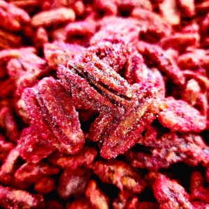 K&ouml;nnte beinhalten: Nahaufnahme von kandierten Pekann&uuml;ssen, die eine satte, r&ouml;tlich-braune Farbe mit einer Zuckerschicht aufweisen. Die N&uuml;sse sind eng aneinandergereiht und f&uuml;llen das Bild aus. Das Bild hebt die Textur und S&uuml;&szlig;e des Snacks hervor.