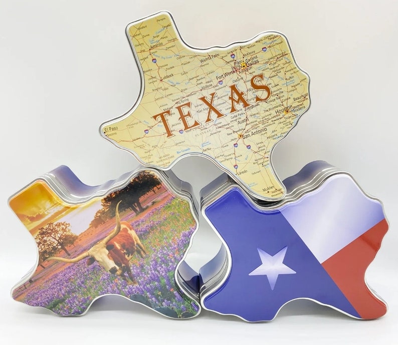 K&ouml;nnte beinhalten: Drei Texas-f&ouml;rmige Dosen. Eine Dose zeigt eine Karte von Texas mit dem Wort "TEXAS". Eine andere zeigt die Texas-Flagge. Die dritte Dose zeigt einen Longhorn in einem Feld mit Lupinen. Die Dosen sind aus Metall.