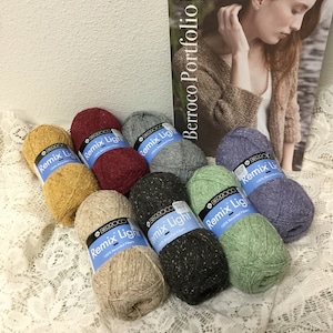 May include: Eight skeins of Berroco Remix Light yarn in various colors, including beige, gray, green, blue, and red. The yarn is 100% recycled fibers.