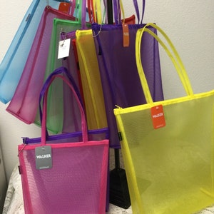 May include: A set of colorful mesh tote bags with zipper closures and the word "WALKER" printed on the front. The bags are hanging on a rack and are available in a variety of colors, including blue, green, purple, yellow, and pink.