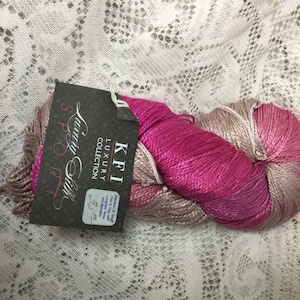May include: A skein of pink and beige yarn with a label that reads "KFI Luxury Collection, Suri & Silk, 50g/220 yds".