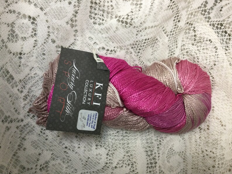 May include: A skein of pink and beige yarn with a label that reads "KFI Luxury Collection, Suri & Silk, 50g/220 yds".