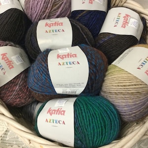 May include: A basket filled with colorful yarn balls. The yarn is labeled "Katia Azteca" and is available in a variety of colors, including brown, blue, green, and beige.