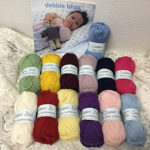 May include: A collection of 14 skeins of Debbie Bliss Baby Cashmerino yarn in various colors, including green, yellow, red, purple, pink, and blue. The yarn is arranged in two rows of seven skeins each.