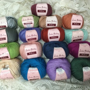May include: A collection of 18 skeins of yarn in various colors, including red, blue, green, purple, and beige. Each skein has a label that reads "Louisa Harding" and "Mulberry".