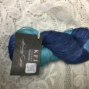 May include: A skein of blue and teal luxury silk yarn from the "Luxury Collection" by KFI. The label reads "KFI Luxury Collection,  Spool Silk, 3.5 oz, 700 yds, 100% Silk, Made in India".