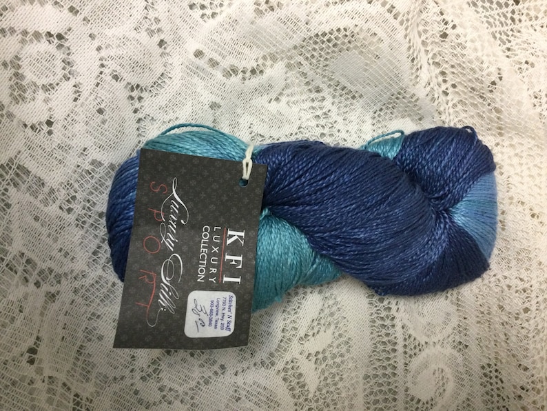 May include: A skein of blue and teal luxury silk yarn from the "Luxury Collection" by KFI. The label reads "KFI Luxury Collection,  Spool Silk, 3.5 oz, 700 yds, 100% Silk, Made in India".