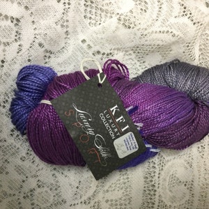 May include: A skein of purple, blue, and gray yarn with a label that reads "KFI Luxury Collection Luxury Silk Sport 32/2".