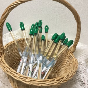 May include: A wicker basket filled with green and gold knitting needles in clear plastic tubes. The tubes are labeled "FlexiFlips" and "FlexiFines Bamboo".
