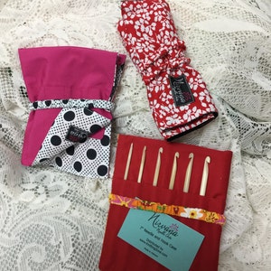 May include: A set of three needle and hook cases. The cases are made of fabric and have different patterns. The red case has a white floral pattern, the pink case has a black polka dot pattern, and the red case has a colorful floral pattern. The cases are designed to hold knitting needles and crochet hooks. The cases are labeled "Nirvana Needle Arts" and "7" Needle and Hook Case".