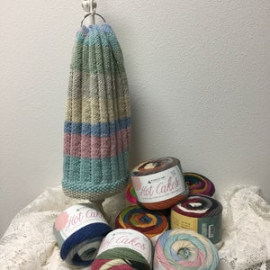 May include: A stack of colorful yarn skeins labeled "Plymouth Yarn Hot Cakes" with a knitted hat in the background.