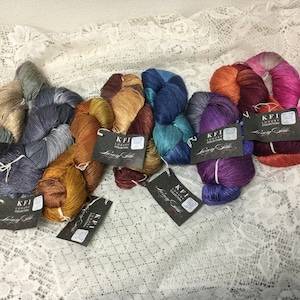 May include: Assortment of colorful skeins of yarn with metallic threads. Each skein has a black tag with the text "KFI Luxury Collection Loving Stitch".