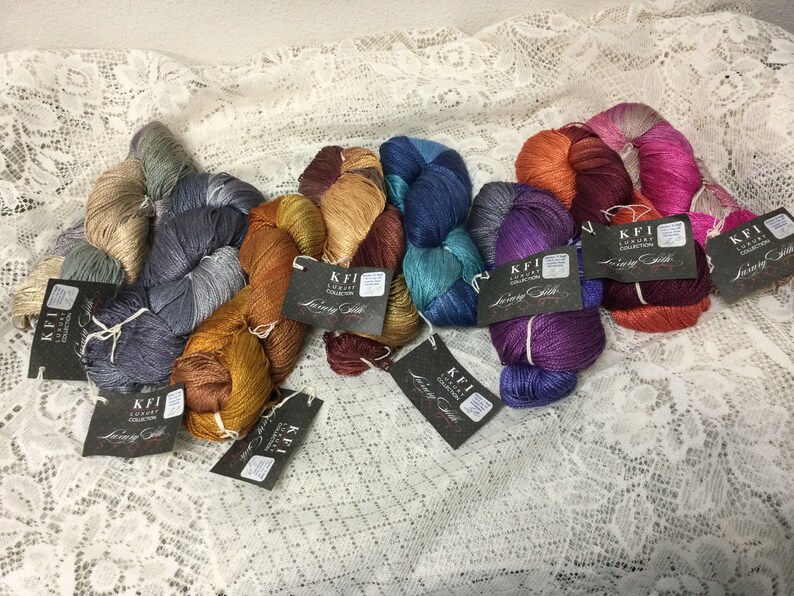 May include: Assortment of colorful skeins of yarn with metallic threads. Each skein has a black tag with the text "KFI Luxury Collection Loving Stitch".