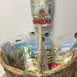 May include: A wicker basket filled with several Amigurumi Kit packages. The kits feature various crochet animal designs, including a bunny, bee, and sheep. The packages are labeled "Easter collection" and "Circulo".