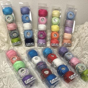 May include: Ten clear plastic rectangular containers, each holding five small round balls of Lizbeth crochet thread in various solid and variegated colors, including shades of blue, pink, green, yellow, red, purple, white, and orange.