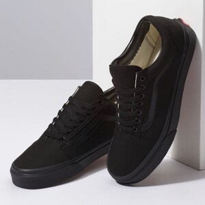 May include: A pair of black canvas sneakers with black laces and a black rubber sole. The shoes have a classic low-top design with a side stripe detail. The sneakers are displayed against a white background.