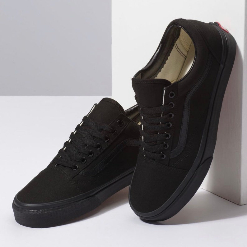 May include: A pair of black canvas sneakers with black laces and a black rubber sole. The shoes have a classic low-top design with a side stripe detail. The sneakers are displayed against a white background.