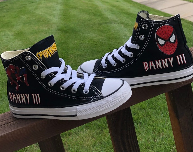K&ouml;nnte beinhalten: Paar schwarze High-Top-Sneaker mit Spider-Man-Grafiken. Die Sneaker haben wei&szlig;e Schn&uuml;rsenkel, Sohlen und Zehenkappen. Der Name "DANNY III" ist rot auf die Seite jedes Schuhs gestickt. Das Wort "SPIDERMAN" ist gelb auf die Zunge gedruckt.