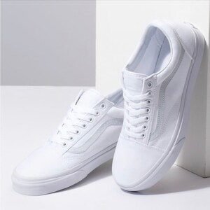 May include: A pair of white canvas sneakers with white laces. The shoes have a classic design with a side stripe and a rubber sole. The sneakers are displayed against a white background.