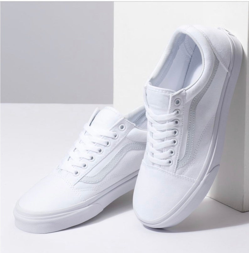May include: A pair of white canvas sneakers with white laces. The shoes have a classic design with a side stripe and a rubber sole. The sneakers are displayed against a white background.