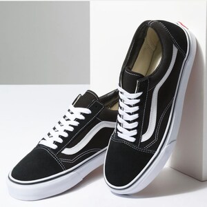 May include: Pair of black and white sneakers with white laces and a white stripe on the side. The shoes have a black suede upper and a white rubber sole. The sneakers are a classic, casual style.