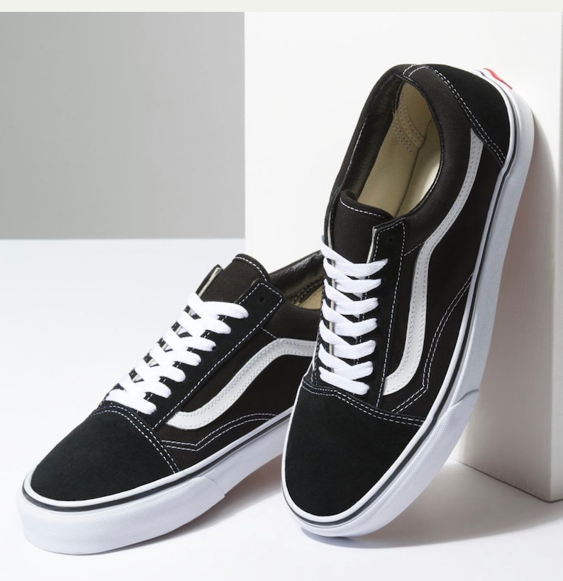 May include: Pair of black and white sneakers with white laces and a white stripe on the side. The shoes have a black suede upper and a white rubber sole. The sneakers are a classic, casual style.
