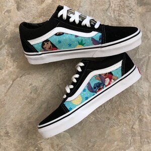 May include: Pair of black and white sneakers with a blue patterned side panel featuring cartoon characters. The shoes have white laces and soles. The design includes images of Lilo and Stitch.