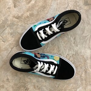 May include: Pair of black and blue Vans Old Skool sneakers featuring a cartoon design. The sneakers have white laces and a white stripe on the side. The design includes characters from a popular animated movie.