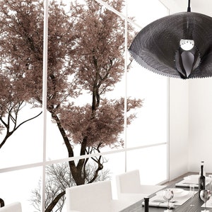 Pode incluir: Uma luminária pendente moderna de malha preta pendura sobre uma mesa de jantar com cadeiras brancas. A luminária tem uma forma orgânica única e está suspensa por um cabo preto. A mesa está posta com pratos brancos, copos e talheres. O fundo apresenta uma janela com vista para as árvores.