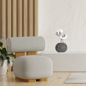 May include: A modern chair with a light gray seat and backrest, set on a wooden base. A decorative sculpture with a textured dark gray sphere base and white and gray looped top sits on a white shelf. The background features a wooden slat wall.