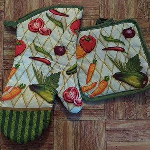 May include: A set of two green and white oven mitts with a vegetable print. The mitts feature a variety of vegetables, including peppers, zucchini, and onions.