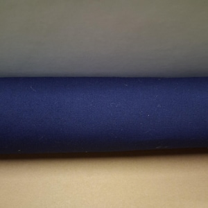 May include: A roll of navy blue fabric. The fabric is tightly woven and appears to be a medium weight material. The fabric is rolled up, showing the texture and color of the material. The background is a light tan color.