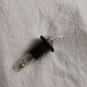 May include: A black and clear plastic bottle pourer with a ribbed base and a clear spout.