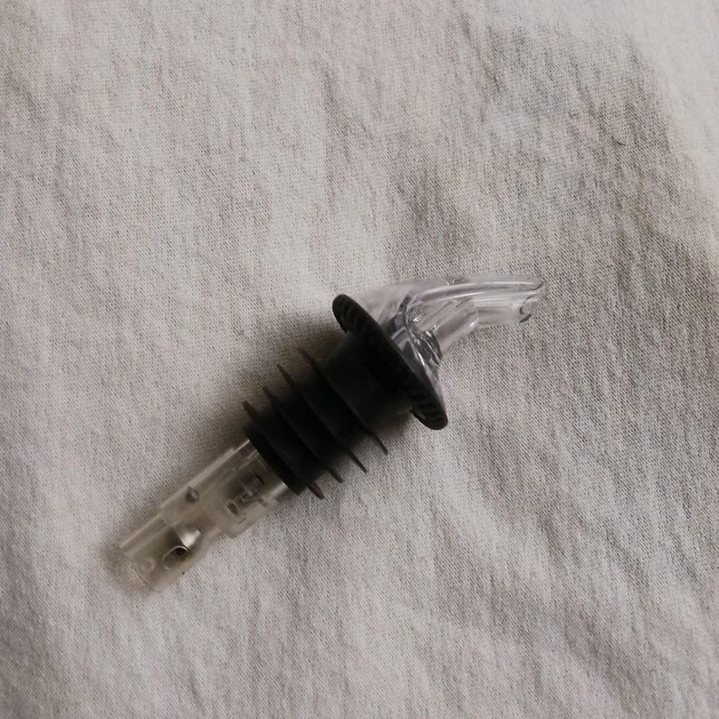 Pu&ograve; includere: Un versatore per bottiglie in plastica nera e trasparente con una base rigata e un beccuccio di versamento trasparente.