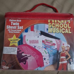 May include: A High School Musical twin sheet set in a clear plastic carrying case with a red zipper and handle. The packaging features text including Cotton Rich, 180 Thread Count, and Deep Pockets, with an image of bedding and two people.
