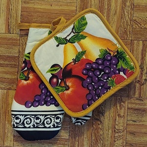 May include: A set of two oven mitts with a yellow trim. The mitts feature a colorful fruit design with pears, apples, grapes, and strawberries. The background is white with a black and white floral border.