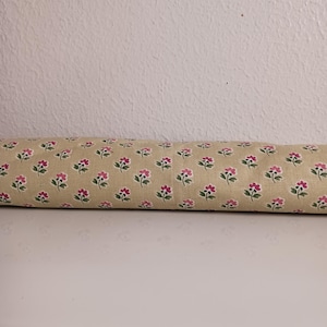 May include: A close-up of a beige fabric with a repeating pattern of small pink flowers with green stems.